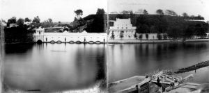 Black-and-white image of an ornate white building on a riverbank with trees behind it