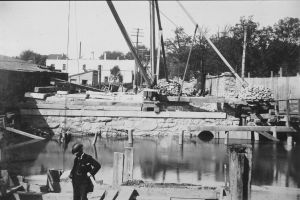 Black and white photo of a man checking his watch in front of a creek with construction around it