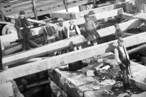 Black and white image of several workmen and many pieces of wooden timber