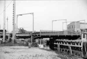 Black and white photo of a drawbridge over a creek, partially opened