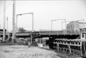 Black and white photo of a drawbridge over a creek, partially opened