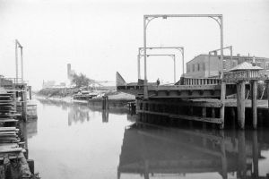 Black and white image of a drawbrige partially opened with water to the left of it