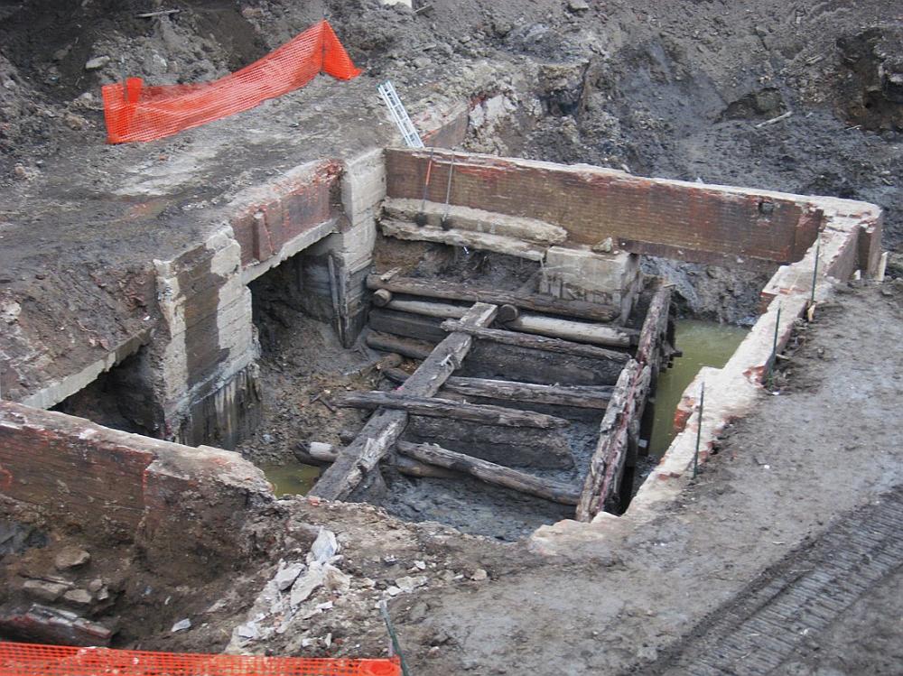 Image shows several excavated wooden poles in a square pen in the mud