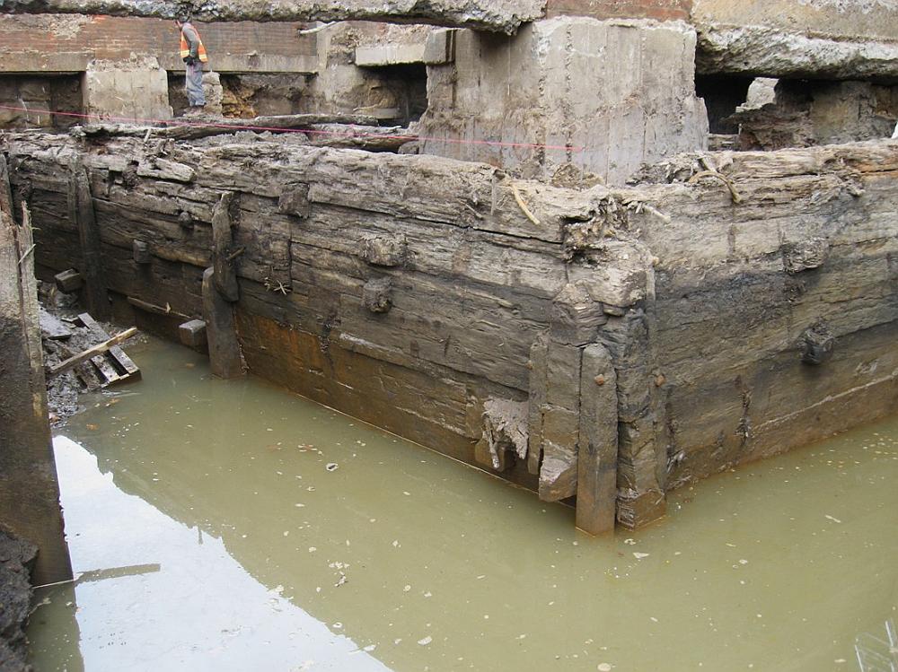 Image shows a large wooden structure in a pool of murky water