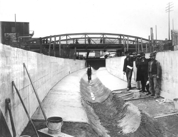Several workers standing against the wall and one walking down the center of the channel, Aramingo Sewer, April 13, 1901