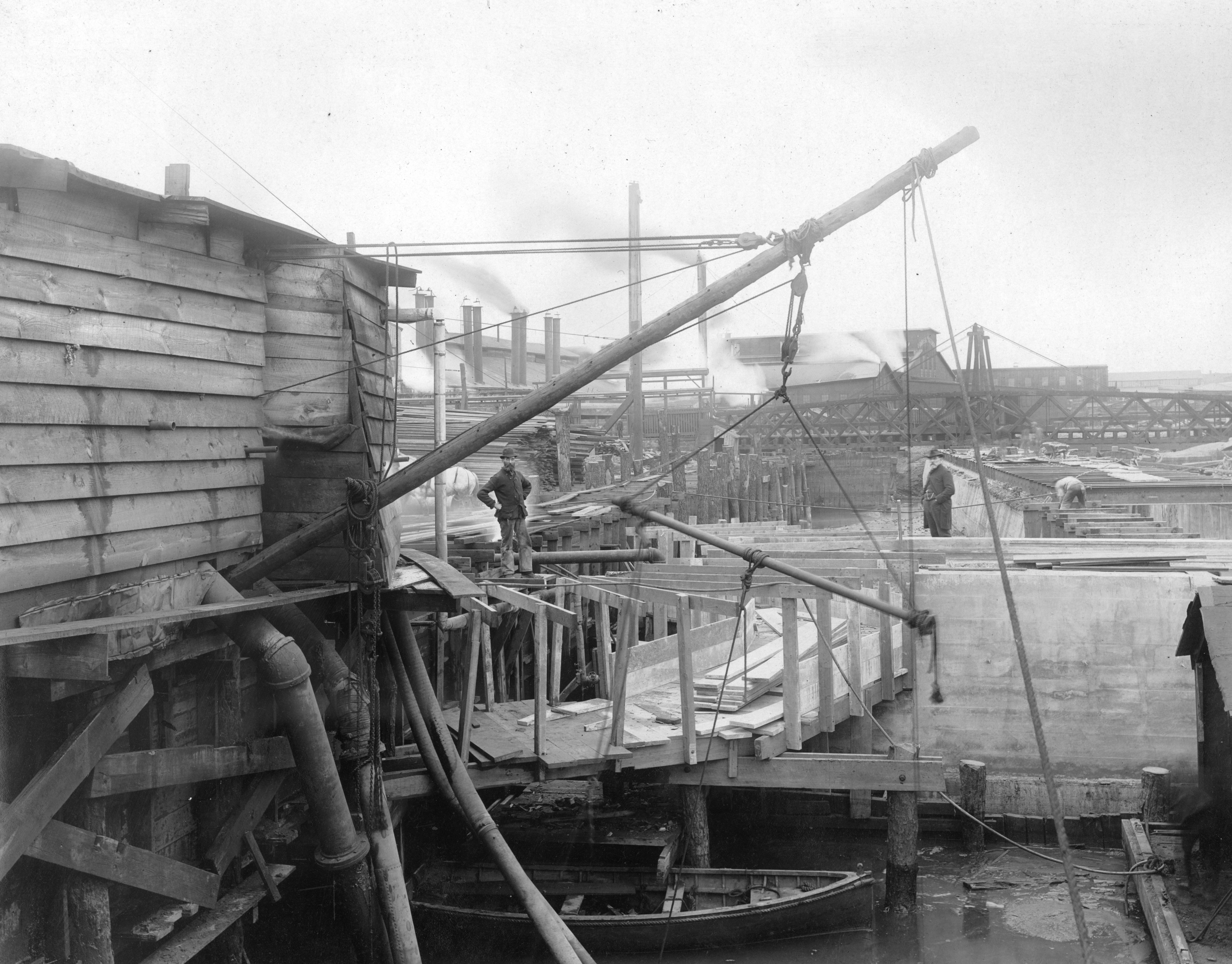 Two men stand on a dock, Delaware River, looking toward the Beach St. Bridge, 1902