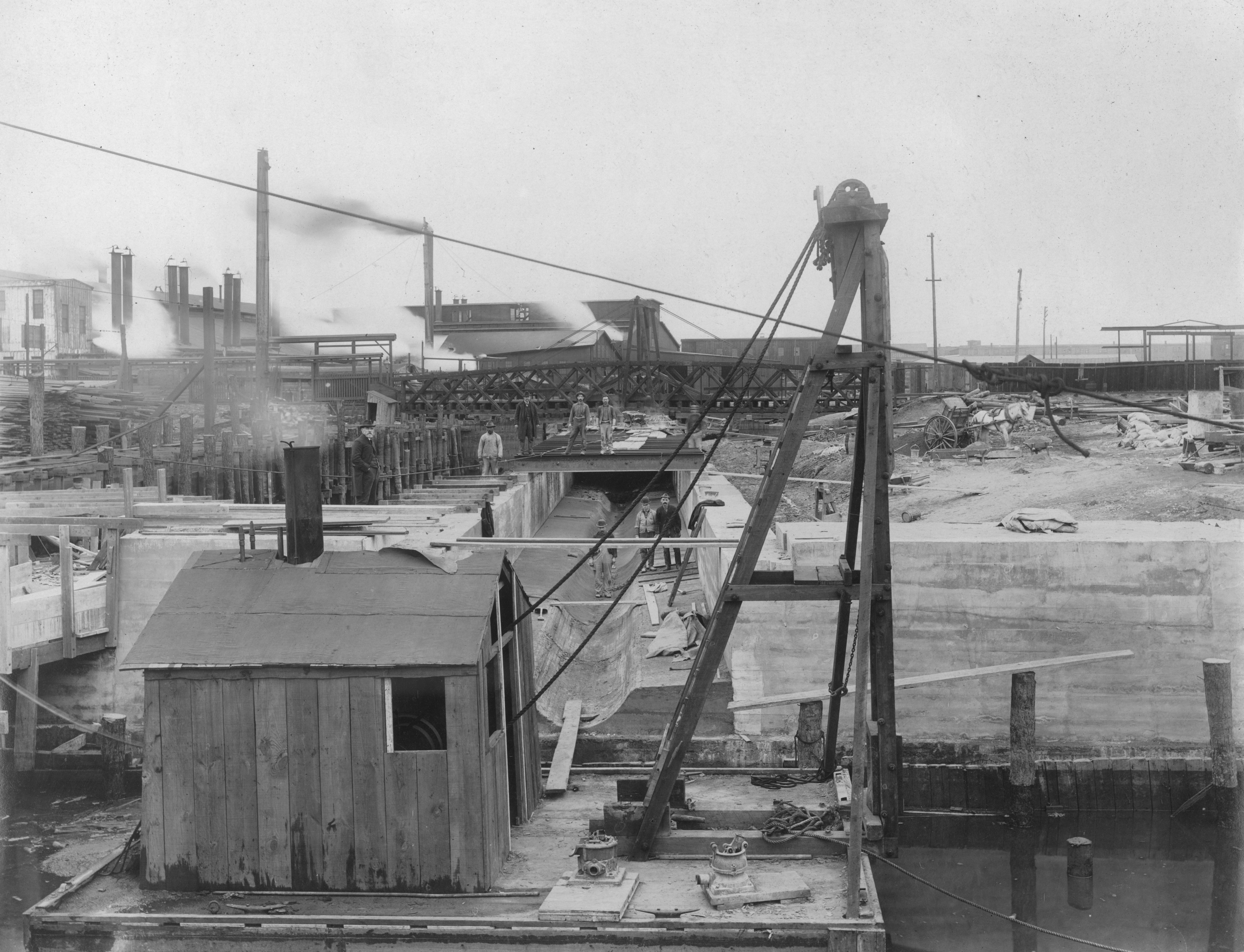 A crane, a shack and some men at the Aramingo Sewer outlet at the Delaware River, 1902