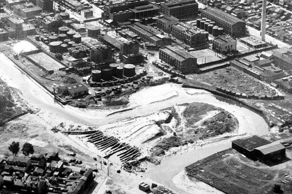 Black-and-white aerial photo of a creek bend with industrial buildings surrounding it