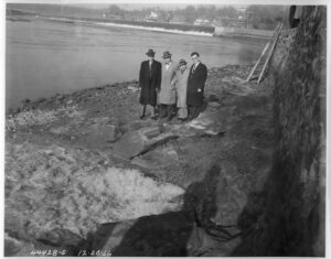 Photo of four men standing on the banks of the Schuylkill River on the last day of the Schuylkill Interceptor, December 20, 1956