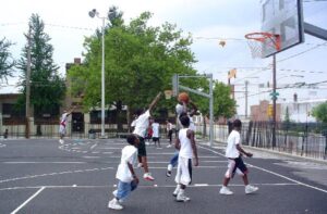 Young men play basketball on a porous basketball court in Mill Creek, Philadelphia