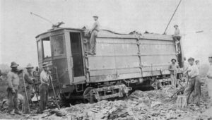 Black-and-white photo of a trolley car atop debris with several workmen around and atop it
