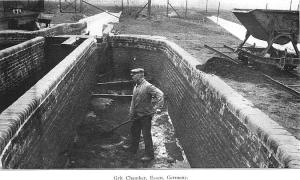 Black-and-white photograph of a man in a hat standing in a brick trench