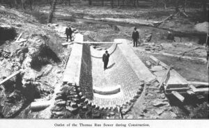Black-and-white image showing a man standing in a large concrete half-pipe
